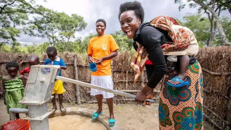 Lachende Frau an einem Brunnen — ein CARE-Wasserprojekt in Sambia